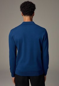 Granatowy sweter z dzianiny z długimi rękawami i kołnierzykiem polo. Posiada ściągacz na dolnym brzegu i mankietach, gładką teksturę oraz dopasowany krój.