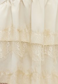 Tissu crème avec deux bandes horizontales de délicate dentelle beige présentant des motifs floraux et géométriques complexes.