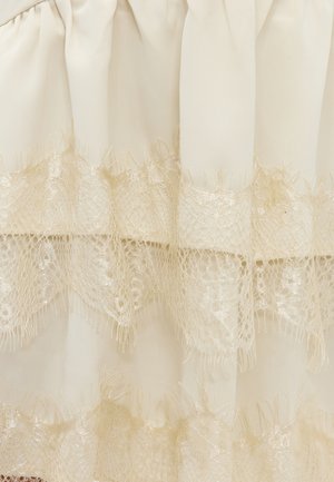Tissu crème avec deux bandes horizontales de délicate dentelle beige présentant des motifs floraux et géométriques complexes.