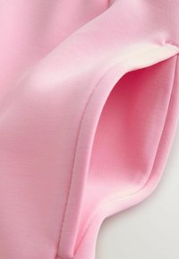 Hele-roosa kangas, millel on sile tekstuur, nähtaval volditud serv ja peened õmblused. Kuju on pehme ja paindlik.