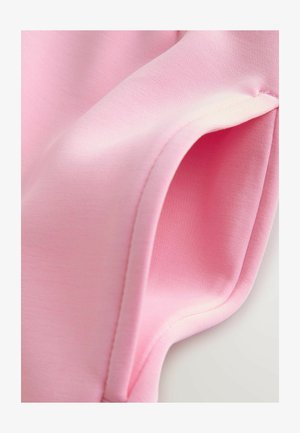 Šviesiai rožinė medžiaga su lygiu paviršiumi, rodanti sulankstytą kraštą ir subtilias siuvimo detales. Forma yra minkšta ir lanksti.