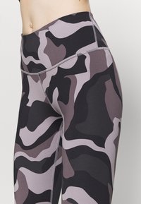 Höga leggings i ett kamouflage-mönster med mörkgrå, ljusgrå och svarta färger. Tillverkade av ett elastiskt material med en sömlös design.