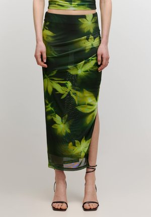 Groene maxi rok met bloemenprint en een zijspleet, gemaakt van lichte stof. Heeft een levendig bladerenpatroon in groene tinten op een donkere achtergrond.