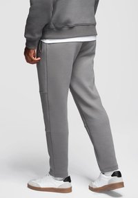 Szare dresy wykonane z miękkiego materiału, z luźnym krojem, bocznymi kieszeniami i ściągaczami u dołu. W zestawieniu z białymi trampkami.