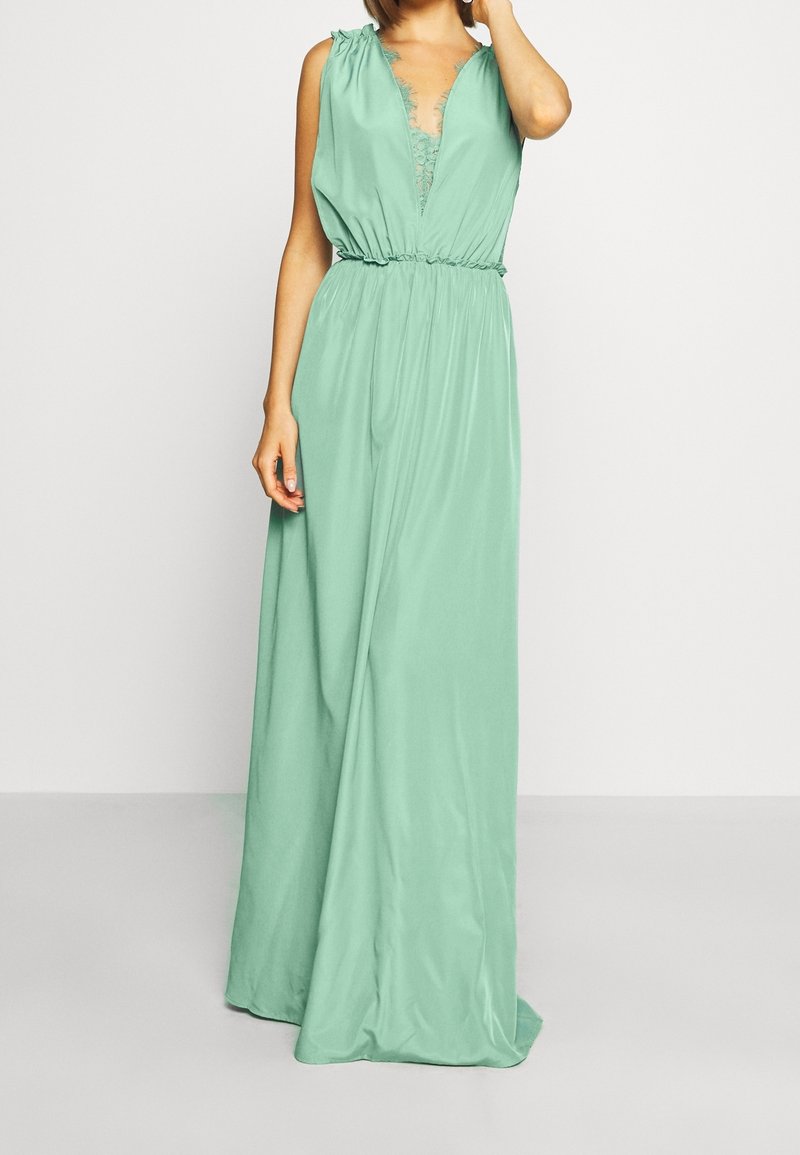 Robe longue sans manches en tissu vert menthe doux. Présente un décolleté en V profond avec des détails en dentelle et une ceinture élastique pour un ajustement décontracté.