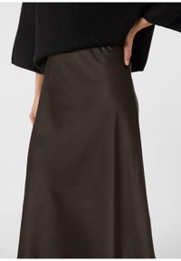 Brązowa spódnica z satyny o gładkiej fakturze, z wysokim stanem i sylwetką w kształcie litery A, zestawiona z luźnym czarnym dzianinowym topem.