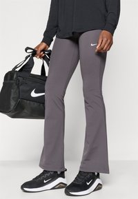 Hallidega laiad spordipüksid, mis on valmistatud venivast kangast, valgete Nike logo aktsentidega, koos mustade Nike jooksujalatsite ja musta spordikotiga.