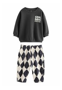Felpa nera con la scritta "COOL DAYS AHEAD" in bianco, abbinata a pantaloni crema con un motivo a rombi neri. Vita elastica sui pantaloni.
