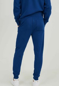 Blue sweatpants made of cotton blend fabric, featuring a tapered design, elastic waistband, and rear patch pocket. Soft texture, plain color.