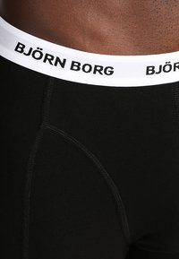 Fekete boxer alsónadrág fehér derékrésszel, amelyen a "BJÖRN BORG" felirat fekete szöveggel látható. Az anyag sima, és látható varrási részletek vannak rajta.