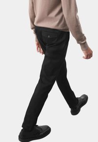 Czarne dopasowane spodnie o gładkiej teksturze, z tylną kieszenią z detalem guzika. W zestawie z czarnymi butami i beżowym swetrem.