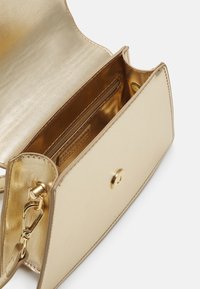 Petit sac à main en cuir beige avec intérieur doré, fermeture pression magnétique et clip de bandoulière amovible, montré ouvert et vide.
