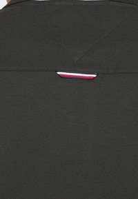 Mörkgrå bomullstyg med ett v-formad halsringning och en liten röd, vit och blå accenttagg nära axelsömmen.