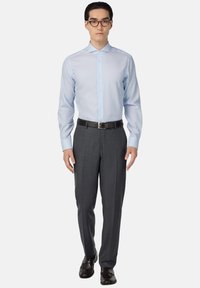 Camicia a righe azzurro chiaro con colletto a punta, abbinata a pantaloni grigi su misura e scarpe nere. La cintura è in pelle marrone scuro.