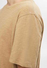Light beige short-sleeve t-shirt made of soft, textured fabric with a crew neckline and clean stitch detailing at the hem and shoulder.