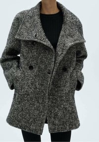 Manteau croisé à motif pied-de-poule noir et blanc. Confectionné en tissu texturé avec un large col et des poches latérales.