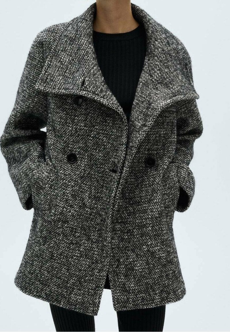 Manteau croisé à motif pied-de-poule noir et blanc. Confectionné en tissu texturé avec un large col et des poches latérales.