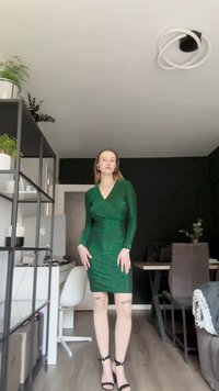 Žalia, prigludusi suknelė ilgomis rankovėmis ir V formos iškirpte, pagaminta iš tekstūruoto audinio. Dėvima su juodais sandalais ant aukštos kulno ir minimaliomis aksesuarais.
