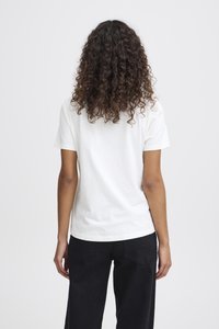 Camiseta de algodón blanca de manga corta, con un cuello redondo y una textura suave, vista desde atrás. Lleva pantalones negros.