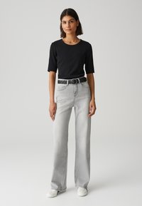Top nero a maniche corte abbinato a jeans larghi grigi chiari. L'outfit è completato da una cintura intrecciata nera e sneakers bianche.