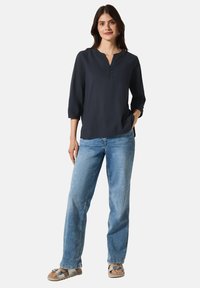 Blusa azul marino de manga 3/4 con escote en forma de pico y tres botones. Combinada con jeans de mezclilla azul claro y sandalias grises con hebilla.