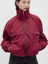 Jachetă roșie cu fermoar, guler înalt, manșete elastice și croială lejeră. Are buzunare frontale și talie strânsă cu șnururi ajustabile.