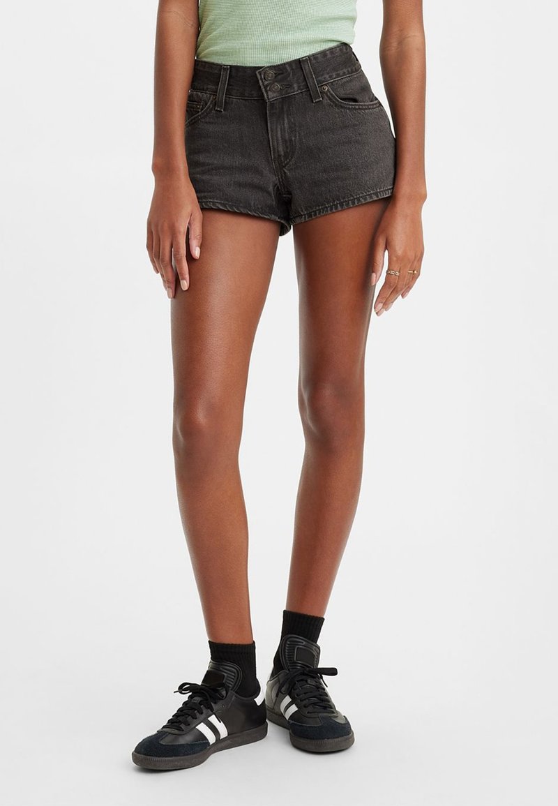Shorts de mezclilla negra con cintura alta, diseño de cinco bolsillos y dobladillo deshilachado. Combinados con zapatillas negras y calcetas negras para hacer contraste.