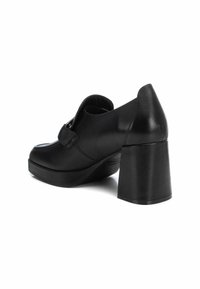 Scarpa nera con tacco alto realizzata in pelle, con punta arrotondata e tacco spesso a blocco. Presenta una fibbia decorativa e una texture liscia.