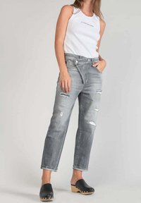 Harmaat kulutetut farkut, joissa on repeämiä, korkeavyötäröiset ja rento istuvuus, yhdistettynä valkoiseen ribbineulottuun toppiin. Mustat puiset puukengät täydentävät asun.