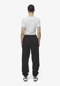Un tricou scurt alb purtat împreună cu o pereche de pantaloni de trening negri, care au un elastic la talie și gleznele manșetate, completat de adidași gri și negri.