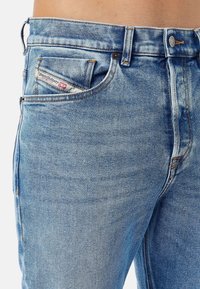 Vaalean siniset farkut viidellä taskulla. Ominaisuuksiin kuuluu keltainen ompelu, metallinappi ja logotagi etutaskussa.