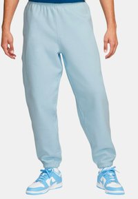 Pantalones de chándal de color azul claro fabricados con una tela suave, con una cintura elástica, tobillos ajustados y bolsillos laterales, combinados con zapatillas azules.