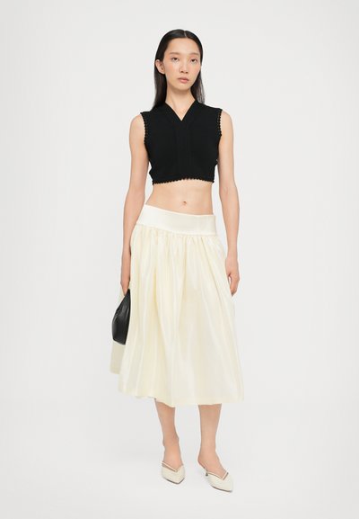 Top negro recortado sin mangas con bordes festoneados, combinado con una falda larga de color crema con una cintura ancha y una textura suave.
