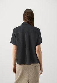 Sort kortærmet skjorte lavet af glat stof med en afslappet pasform, der har en lige rygsaum og et klassisk kravedesign.