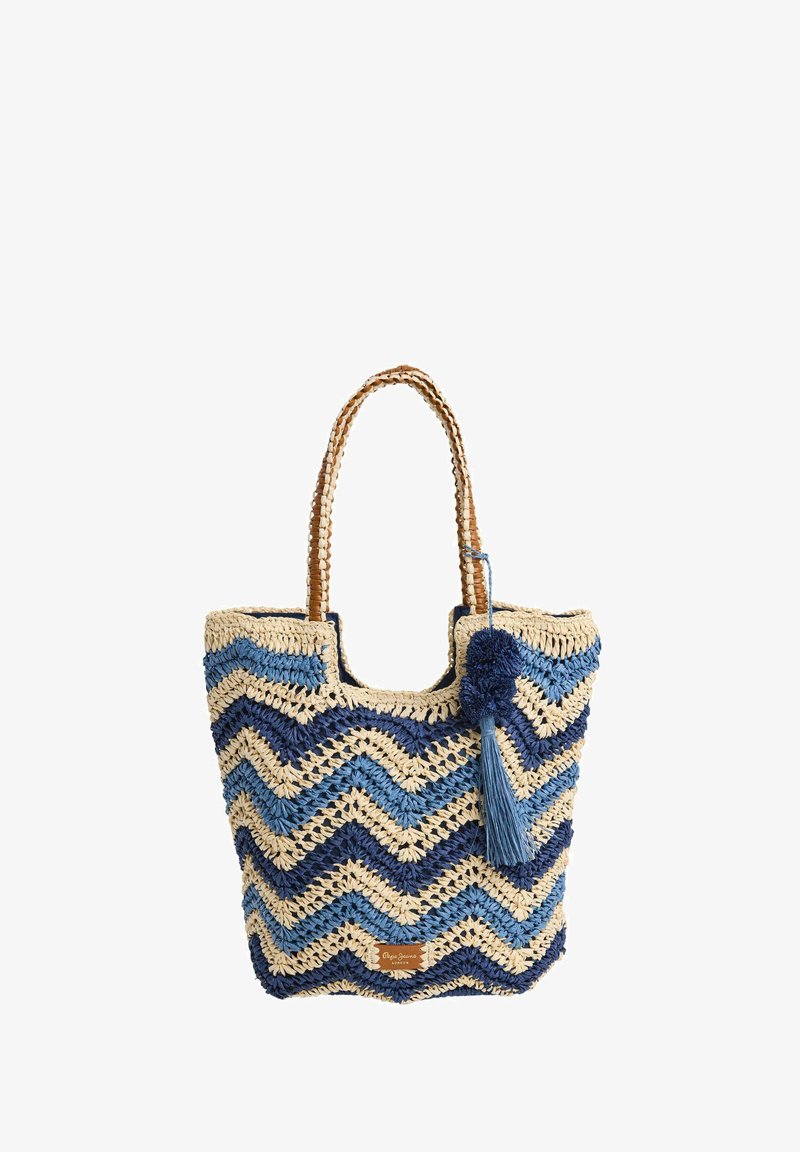 Vävd strandväska med blå och beige zigzag-mönster, en texturerad yta och dekorativa pom-pom- och tofsdetaljer.