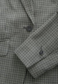 Hall triibuline bleiser, mis on valmistatud tekstuurse villasegust materjalist, kahe musta nupuga mansettidel ja klassikalise sälglapiga disain.