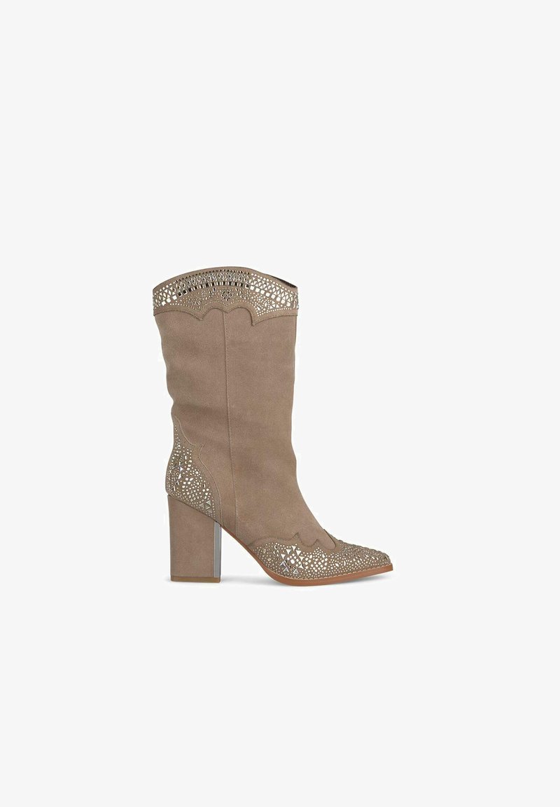 Bottes à talons hauts en suède beige avec des détails découpés au laser complexes au col et à l'embout, avec un design sculpté et un accent métallique.