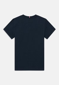 T-shirt de manga curta em azul marinho escuro com um pequeno detalhe listrado em vermelho, branco e azul na parte de trás do decote, disposta de forma plana mostrando as costas.