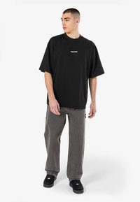Černé bavlněné oversize tričko s bílým logem na hrudi. Kombinováno se šedými denimovými kalhotami a černými sneakers, což podtrhuje ležérní vzhled.
