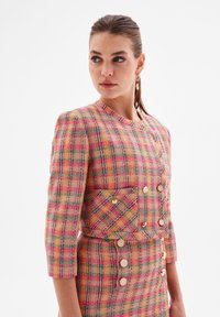 Tweed blazer and skirt set featuring a multicolored check pattern in pink, green, and yellow, with rectangular pockets and round buttons.
