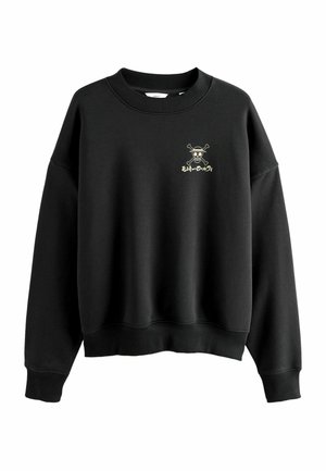 Black sweatshirt with ribbed neckline and cuffs. Features a small white and gold skeleton design at the chest. Soft texture, relaxed fit.