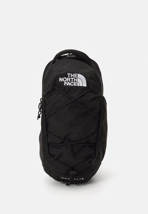 Black backpack with a textured finish, featuring a white logo, bungee cord design on the front, and adjustable padded straps.