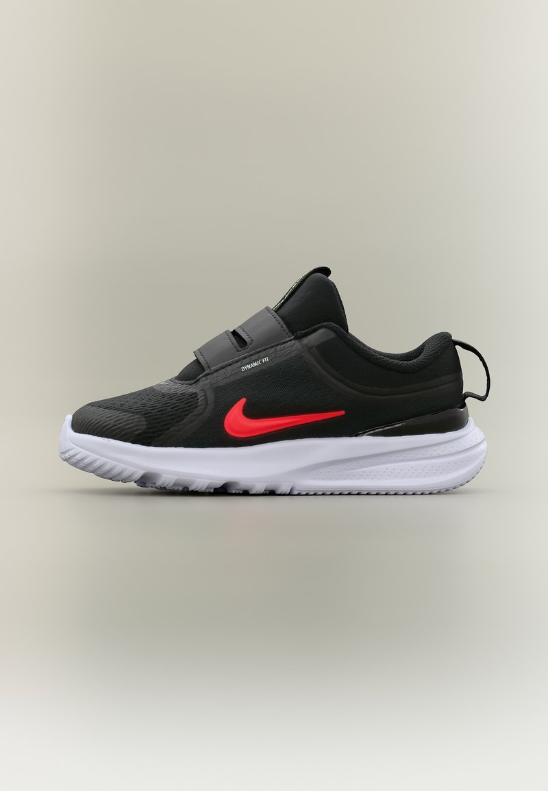 Μαύρο αθλητικό παπούτσι με λευκή σόλα, κόκκινο λογότυπο Nike, επάνω μέρος από δίχτυ, δύο ιμάντες με βέλκρο και θηλιά στο πίσω μέρος, σε απλό φόντο.