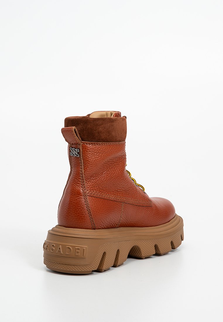Brown leather ankle boot with a textured finish, yellow laces, suede accents, and a chunky brown rubber sole. Features a logo on the side.