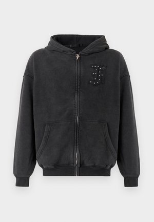 Black zip-up hoodie made of soft, textured fabric. Features a hood, front pockets, and a decorative “J” with studs on the left chest.