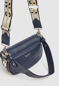 Mörkblå läderaxelväska med en strukturerad yta, som har en framträdande logotyp, silverfärgad hårdvara och en mönstrad justerbar rem.