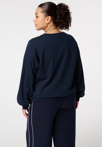 Marineblauwe sweatshirt met lange mouwen, in een ontspannen pasvorm en geribbelde zoom. Kenmerken zijn een zachte textuur en ronde halslijn, gecombineerd met high-waisted broeken.