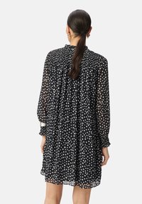 Vestido negro con lunares, de mangas largas, escote fruncido y puños elásticos. Tejido transparente con una forma fluida.