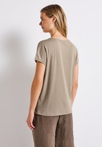 Beige pruhované tričko s krátkým rukávem a kulatým výstřihem, spárované s volnými hnědými kalhotami, z pohledu zezadu. Hladká textura.