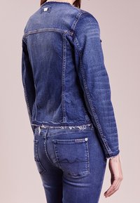 Mörkblå jeansjacka med fransat nederkant, spetsig krage och subtila sömdetaljer. Mörkblå jeans med synliga bakfickor.